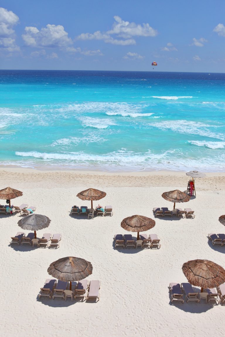 Rows of beach loungers and thatched umbrellas on a white sandy beach in Cancun, Mexico.