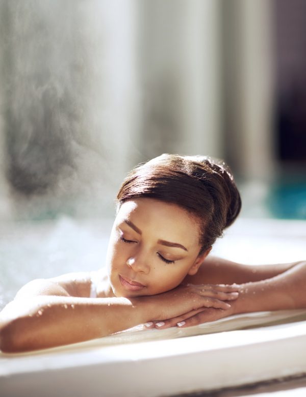 Woman resting with eyes closed on the edge of a steamy spa pool.