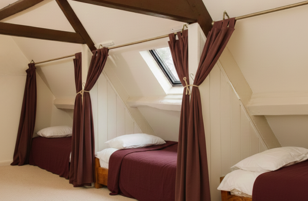 Shared sleeping area with single beds separated by privacy curtains under exposed wooden beams.